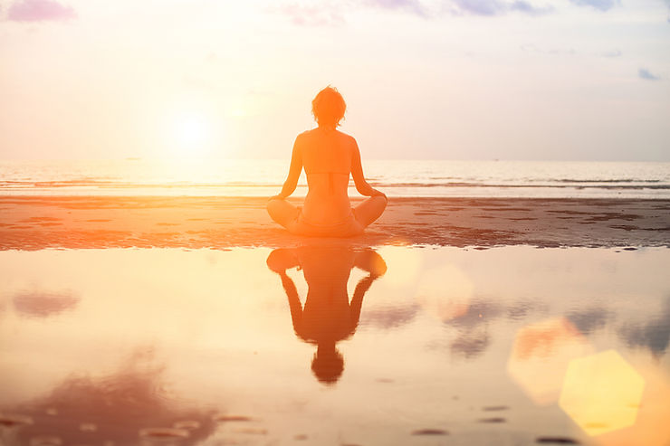 a person sitting in a lotus position on the beach.
